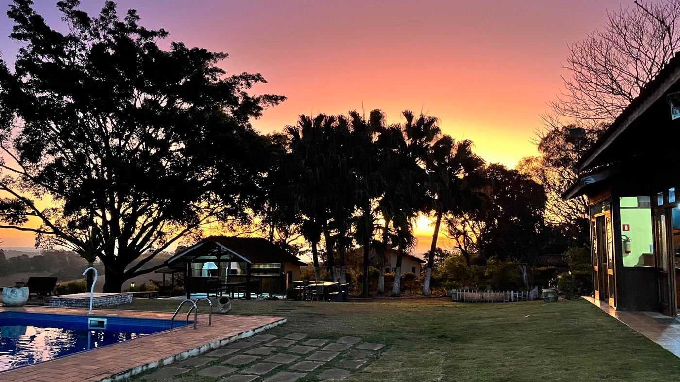 Piscina panorâmica do Recanto das Seriemas com espreguiçadeiras, guarda-sol e palmeiras — pousada na Serra do Itaqueri