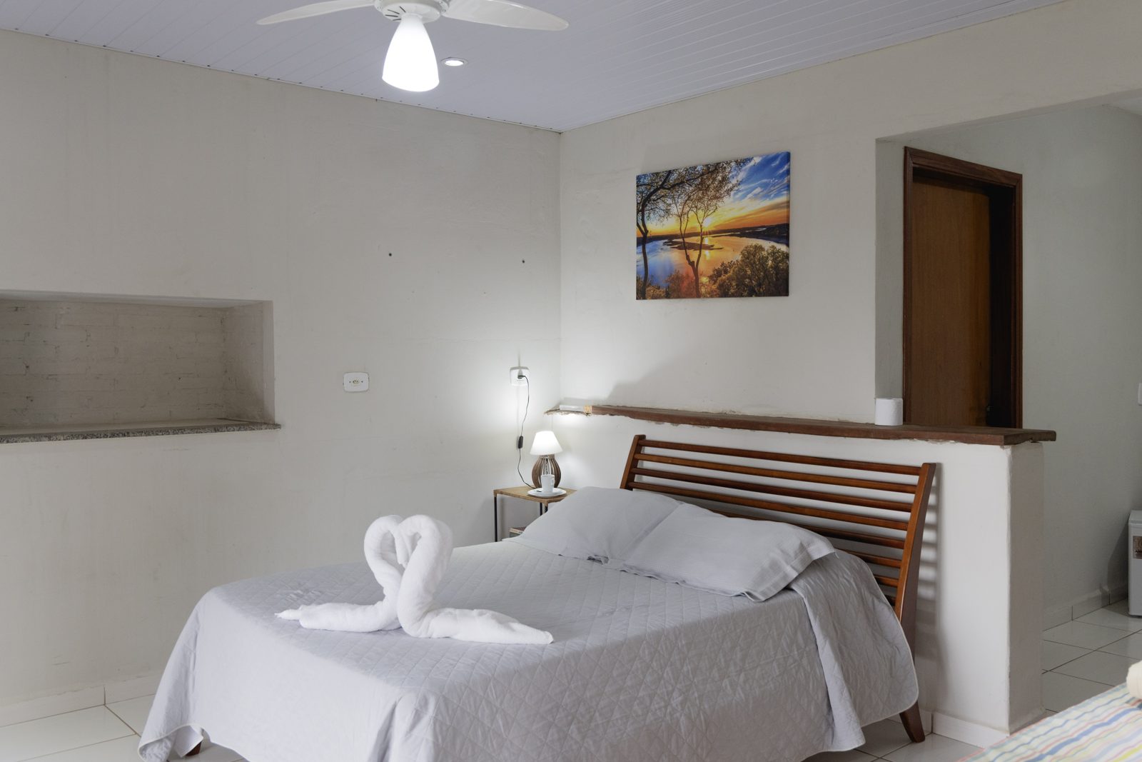 Quarto aconchegante da suíte com luminária de cabeceira e enxoval branco — Recanto das Seriemas